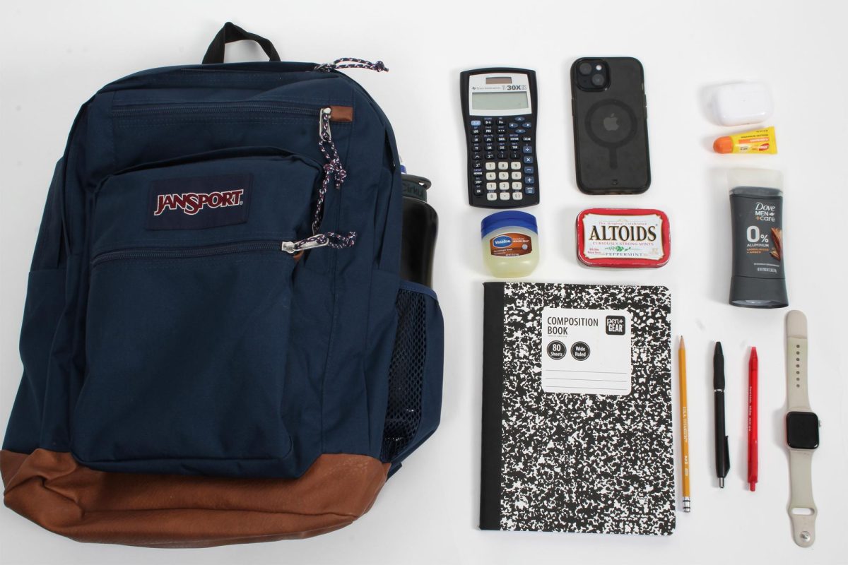 Blue Jansport backpack laid out with pencils, pens a notebook, calculator, vaseline, Airpods, Altoids, a watch, a deodorant, phone and Carmex.